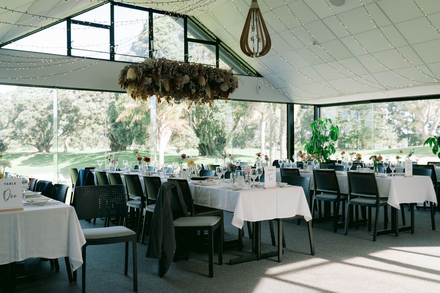 Modern wedding reception venue with floor-to-ceiling windows and elegant white table settings.