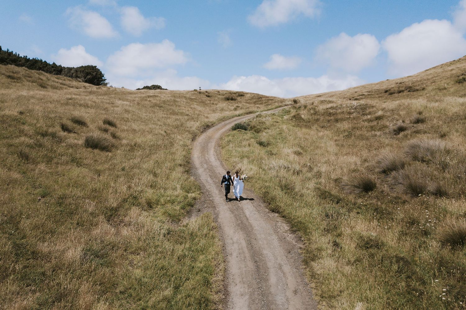 A dirt trail winds through golden hillsides under blue sky as two people walk along the winding path.