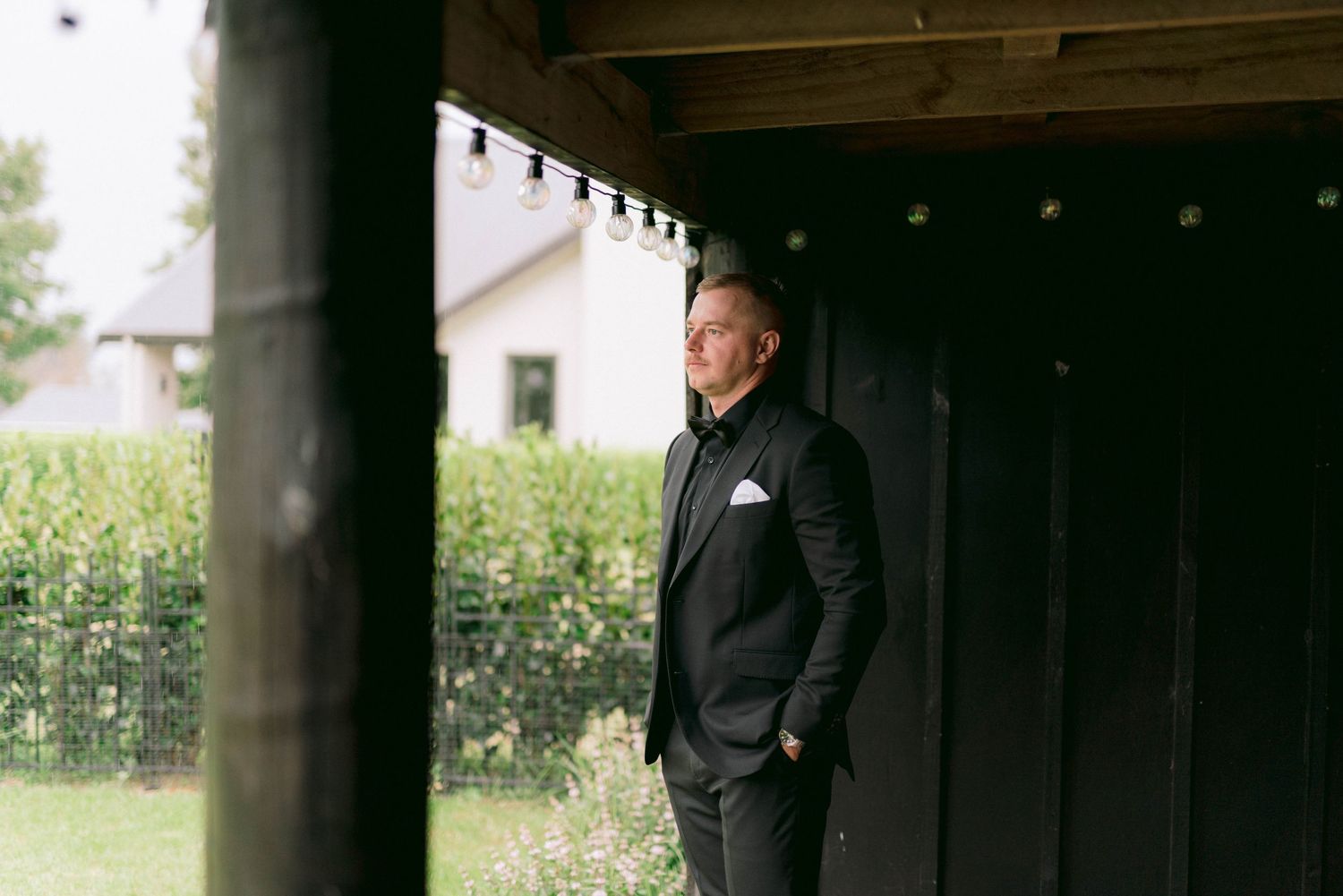 A person in dark clothing stands alone in a shaded outdoor walkway or corridor with pillars.