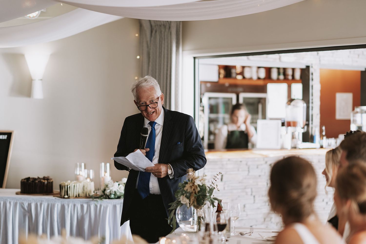 A panoramic view of wedding guests seated at tables during a reception celebration inside an elegant dining room.