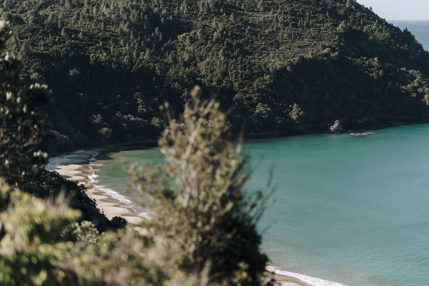 Turquoise ocean waters meet rugged coastal cliffs on a remote coastline under cloudy skies.