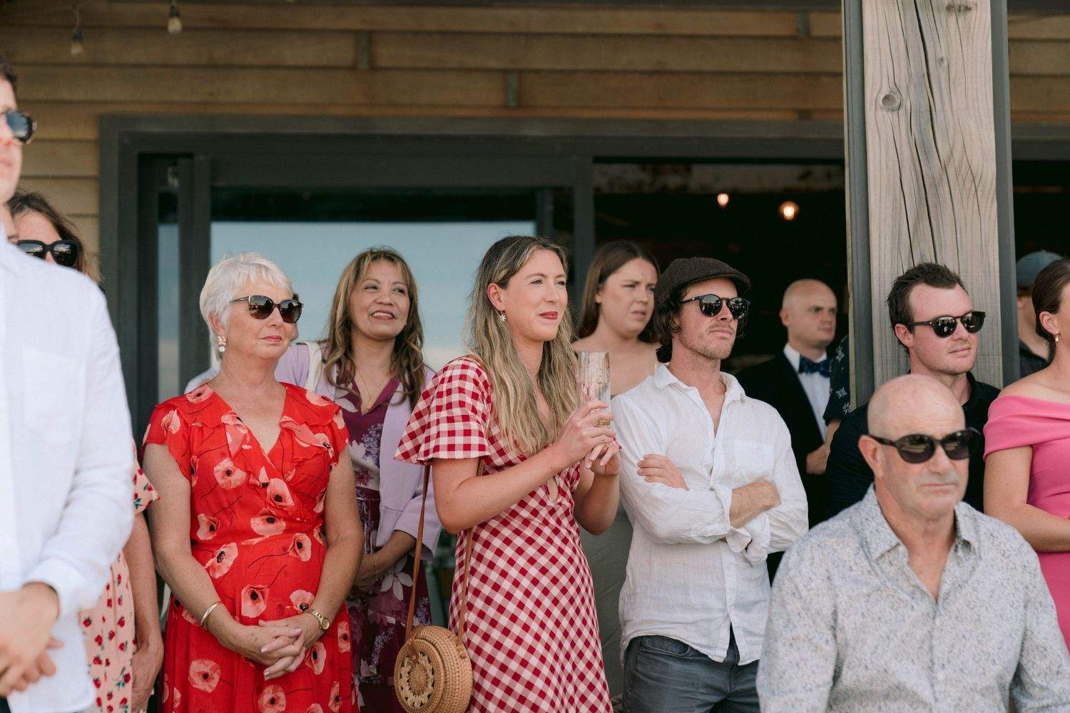 People gathered on a porch wearing summer attire including red dresses and gingham patterns for an outdoor event.