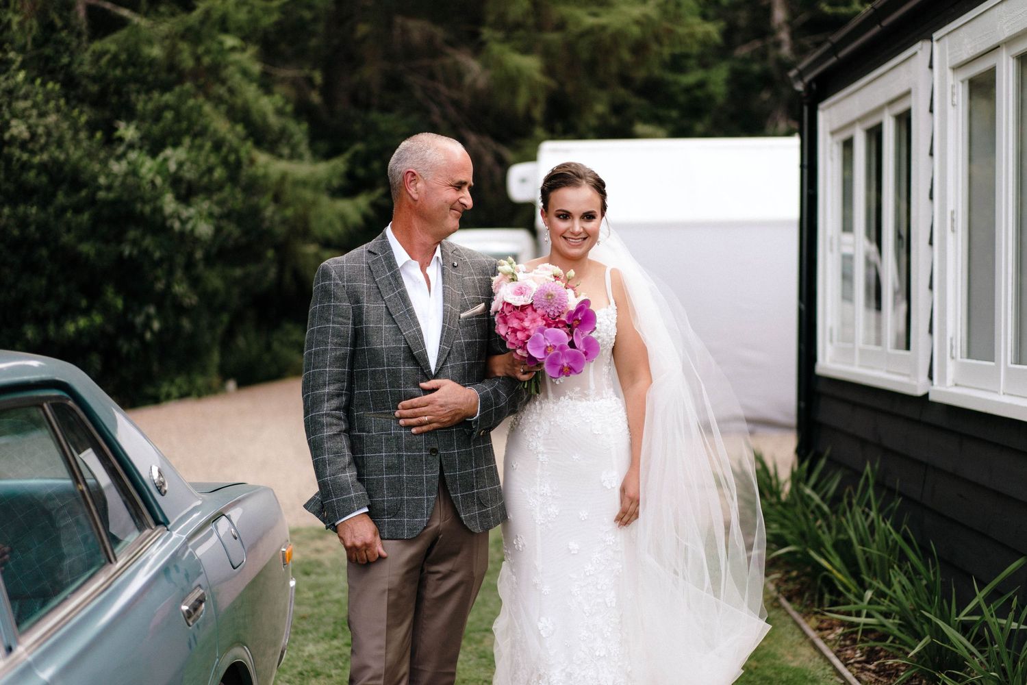 Wedding couple standing outside black and white building with vintage car.