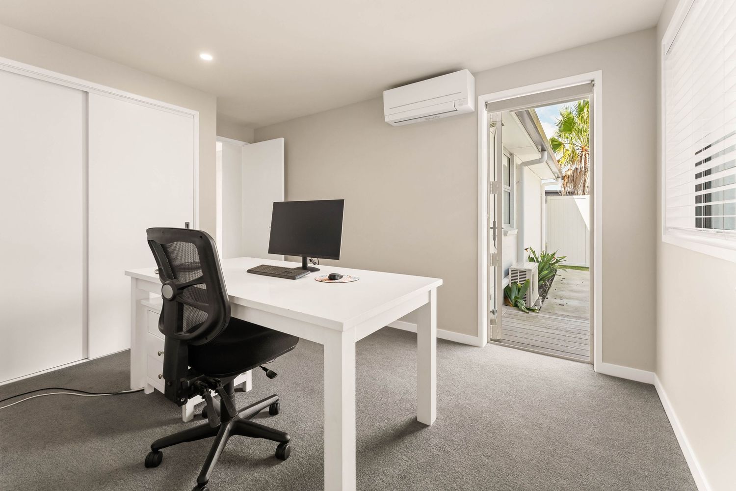 Home office space with ergonomic chair, white desk and carpeted flooring.