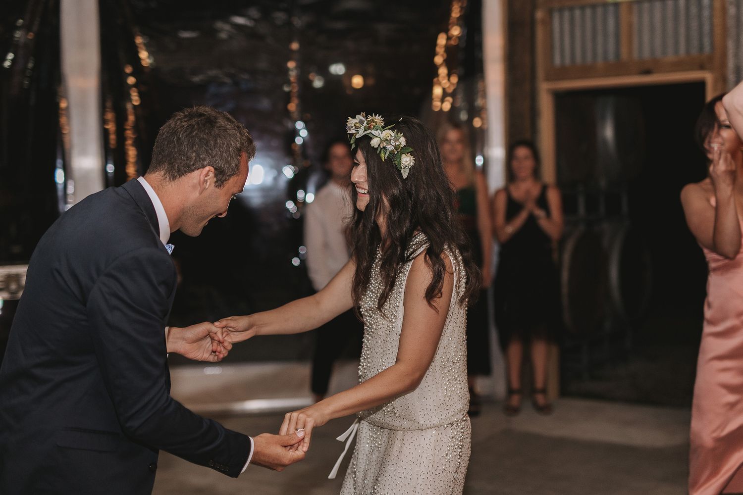 A couple having their first dance on an outdoor wedding dance floor surrounded by guests and string lights.