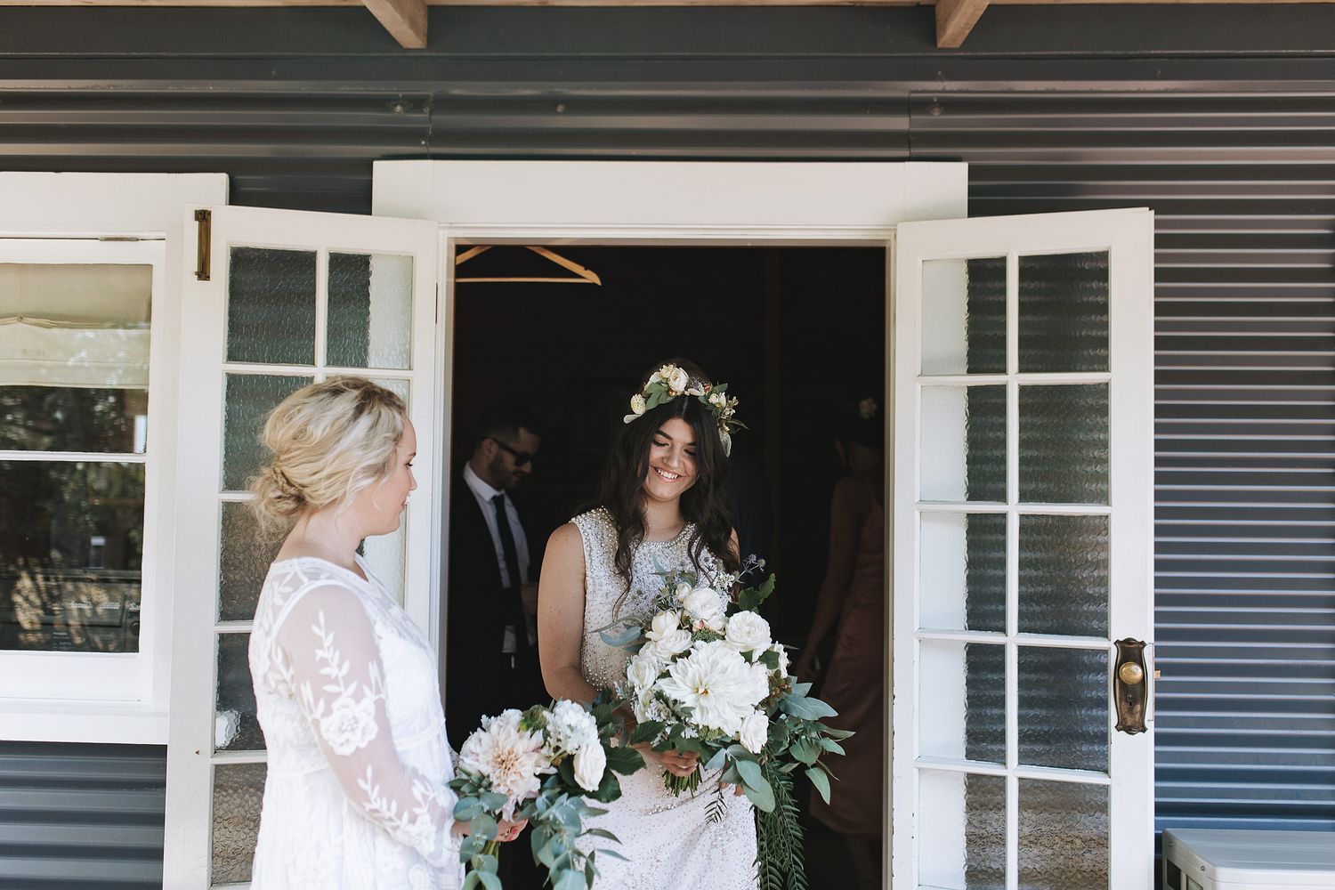 Two people stand in a doorway holding white floral bouquets at an elegant outdoor venue.