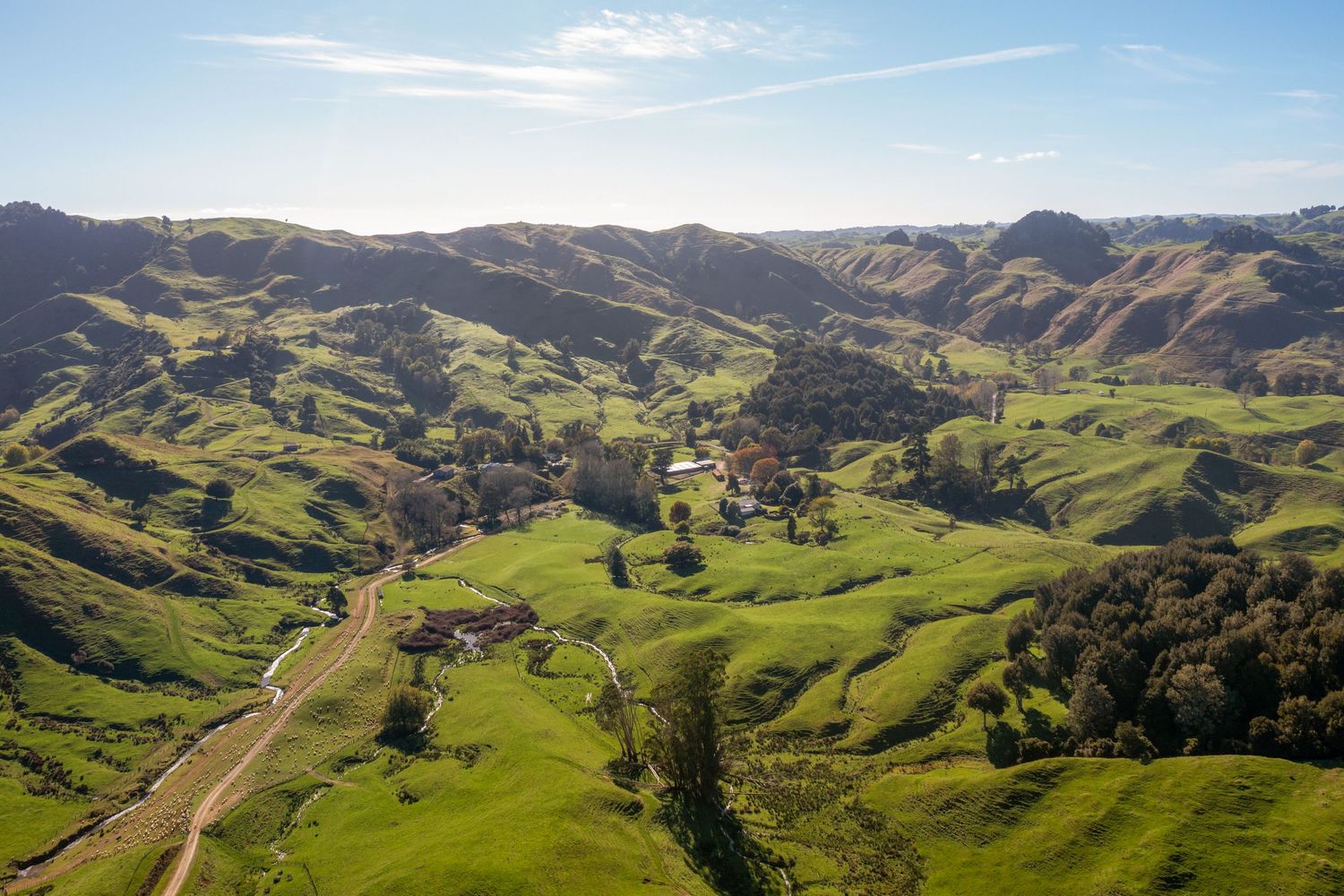 Aerial view of rolling green hills and winding roads through a scenic pastoral valley in rural countryside.