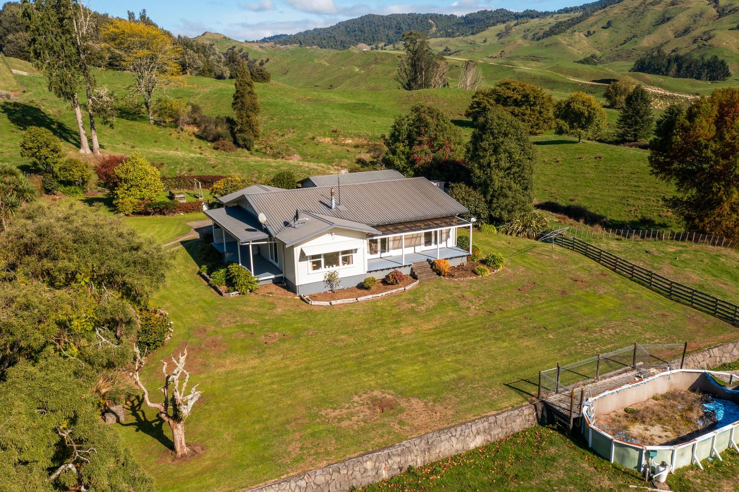 Modern ranch house with grey roof on hillside property featuring circular swimming pool.