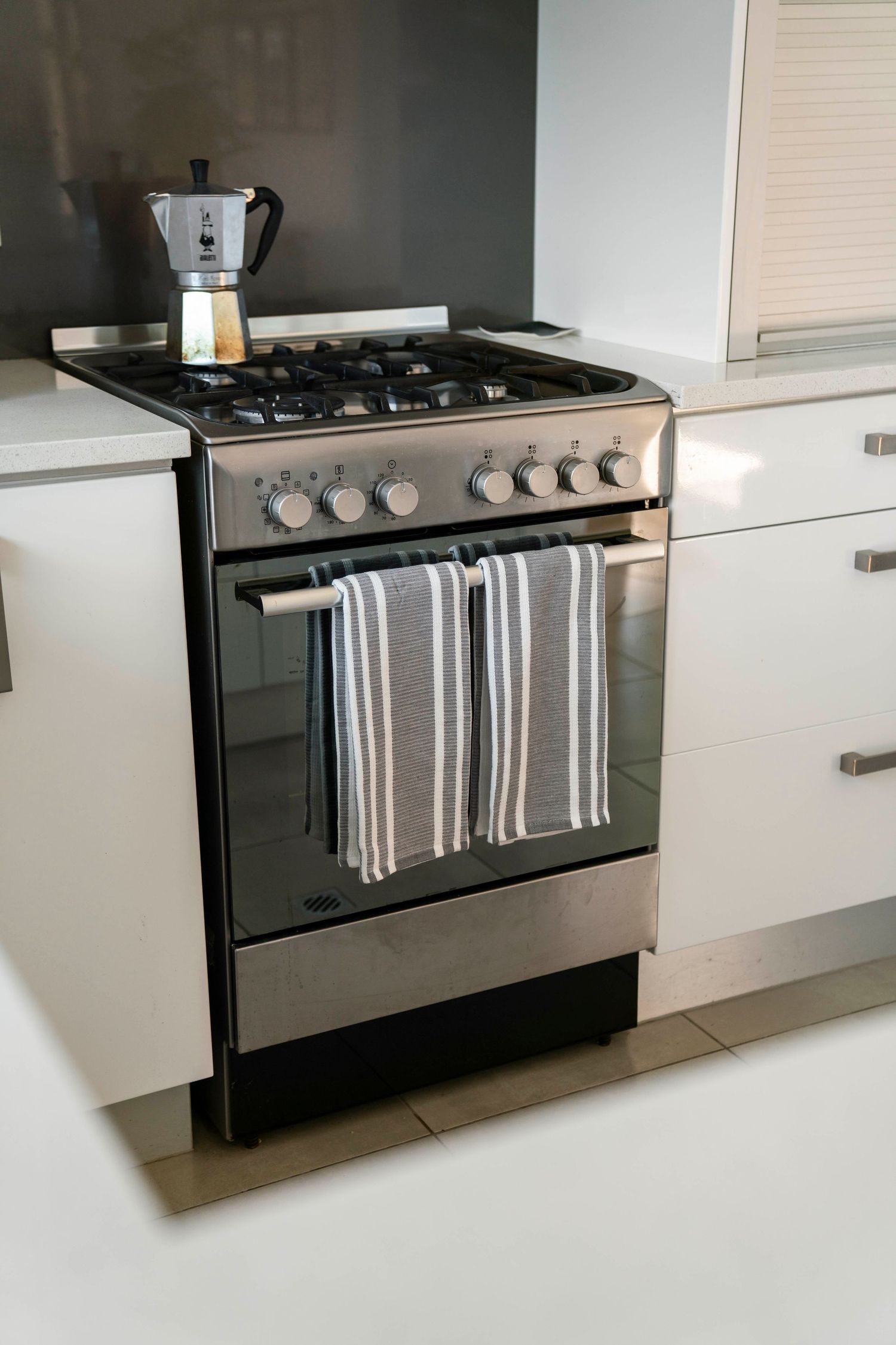 Modern kitchen featuring black gas stove with striped tea towels hanging from handle against white cabinetry.