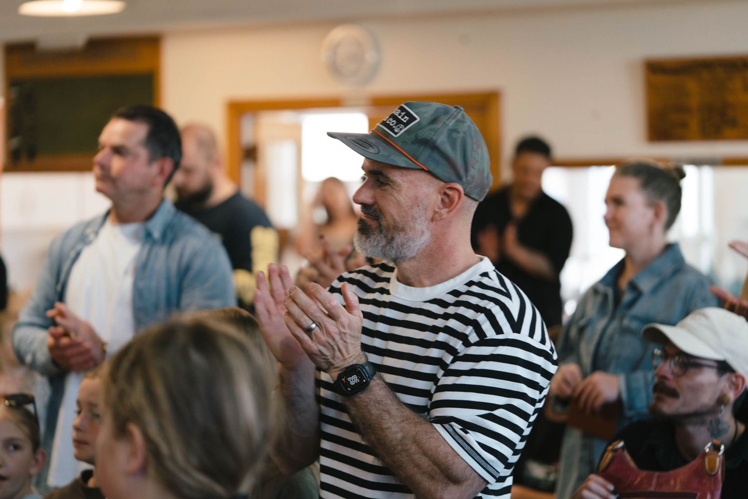 People gathered in a wooden-paneled room with pendant lighting for what appears to be a community event.