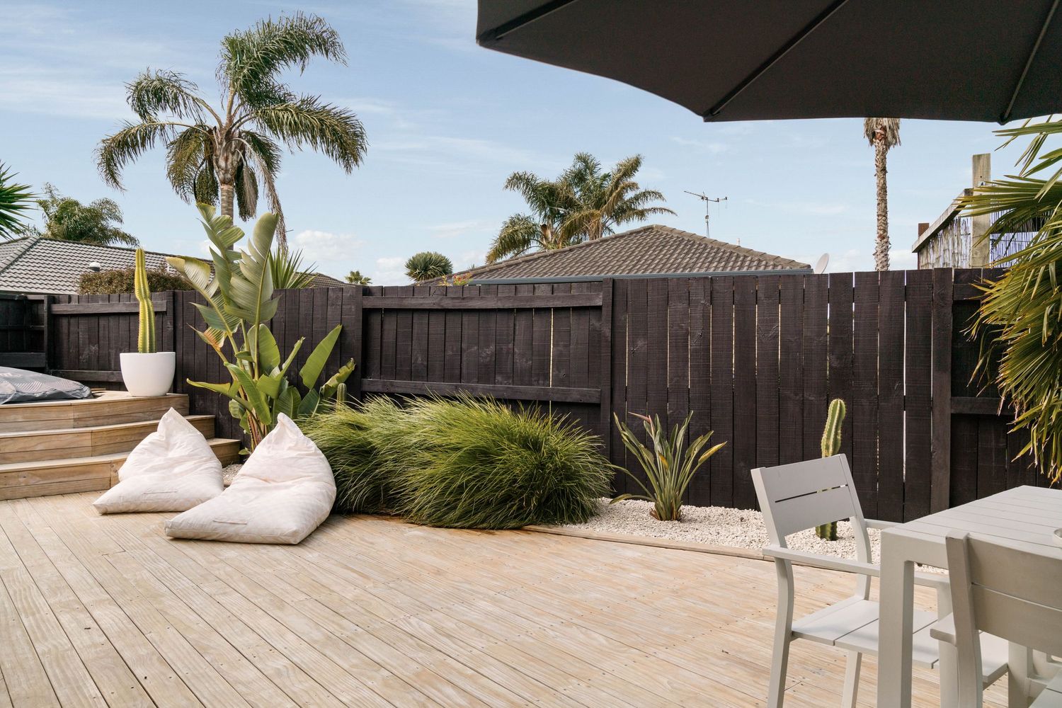 Coastal backyard deck with palm trees, wooden fence, white bean bag chairs and outdoor furniture.
