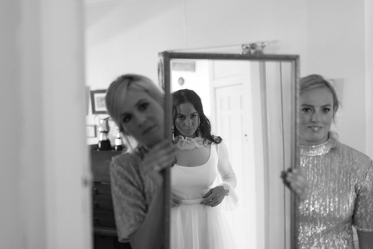 Black and white photo of people in formal attire getting ready in a room with a doorway and mirror.