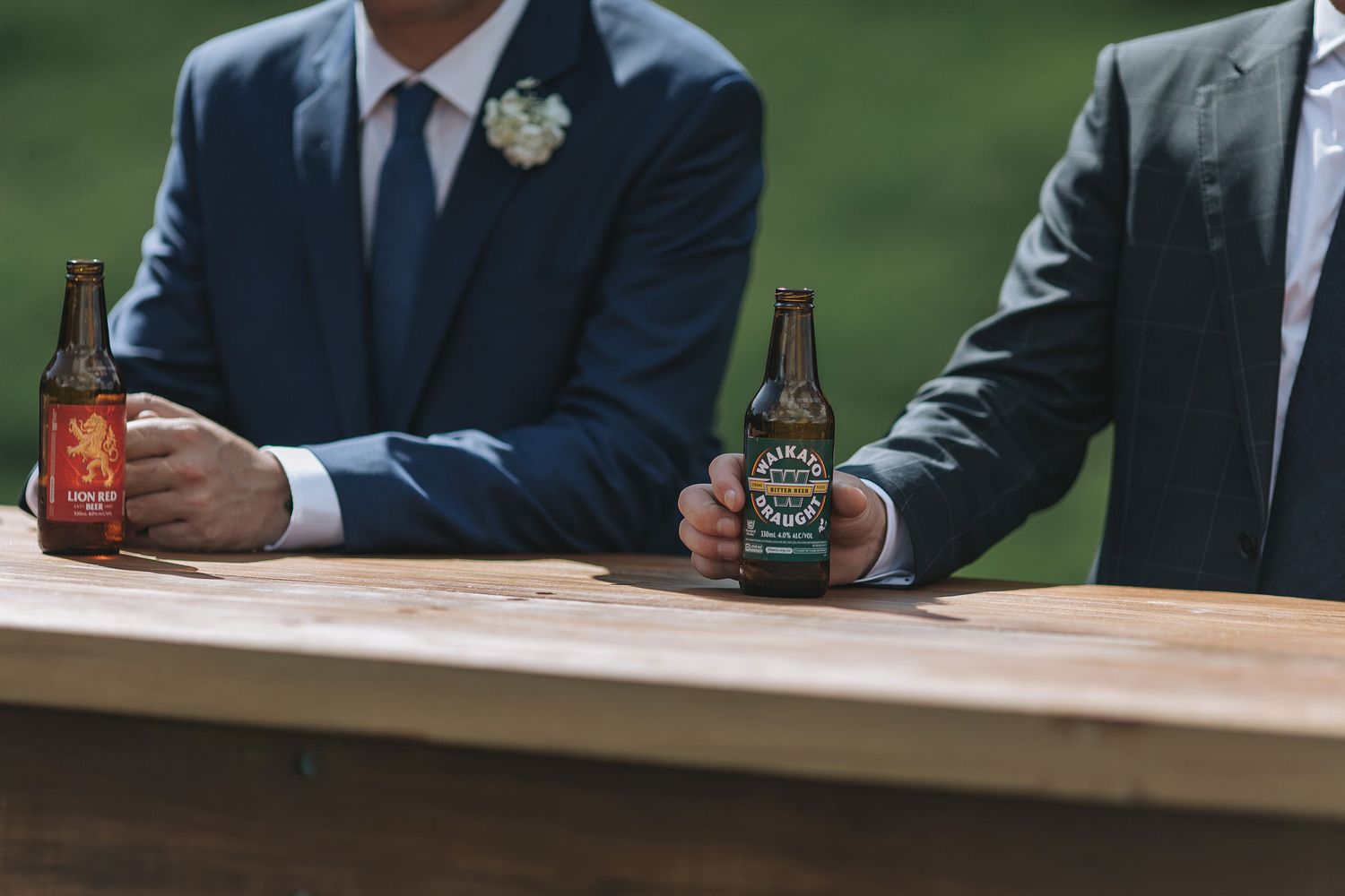 People toasting with beer bottles and drinks at a rustic wooden table during a celebration event.
