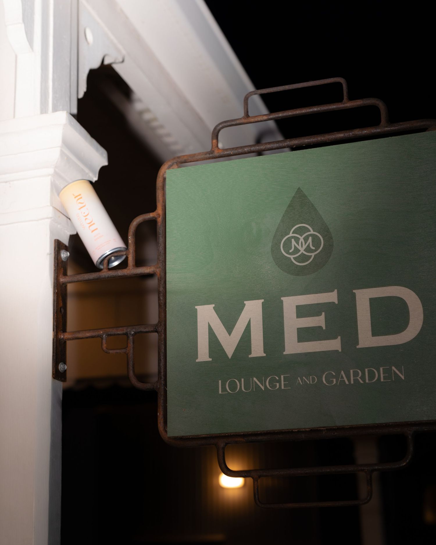 A vintage-style green sign reading 'MED LOUNGE AND GARDEN' mounted on a wall at night.