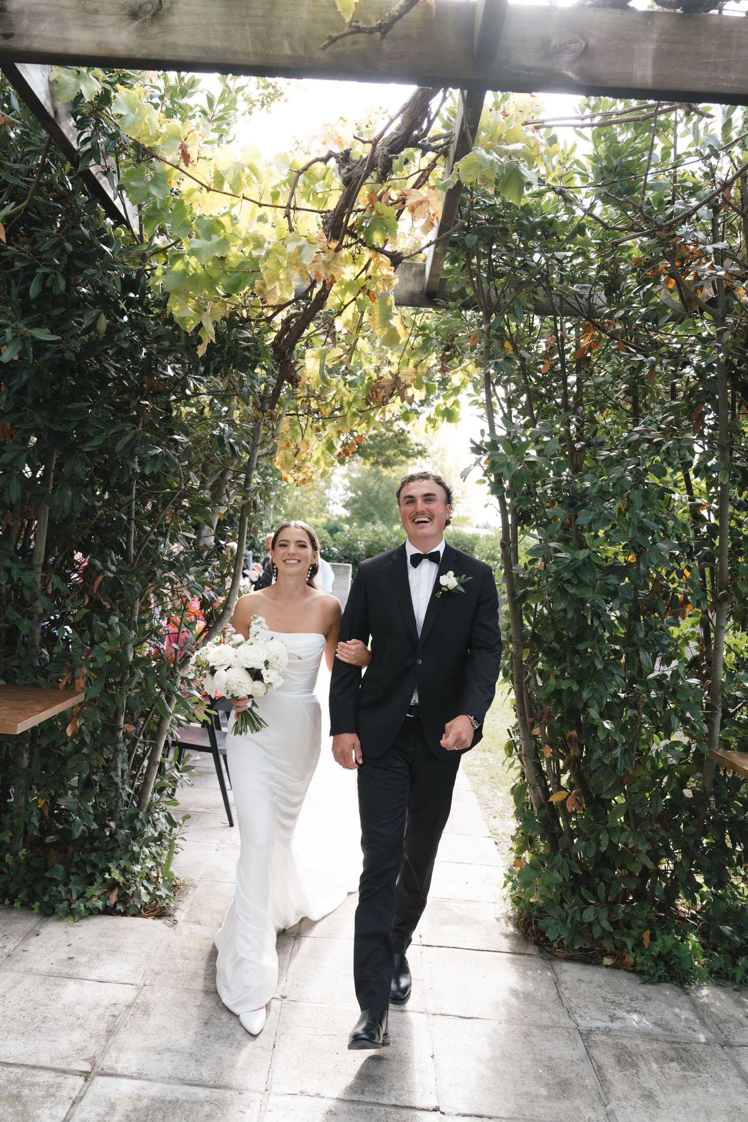 A couple walking through a lush garden archway during their wedding celebration.