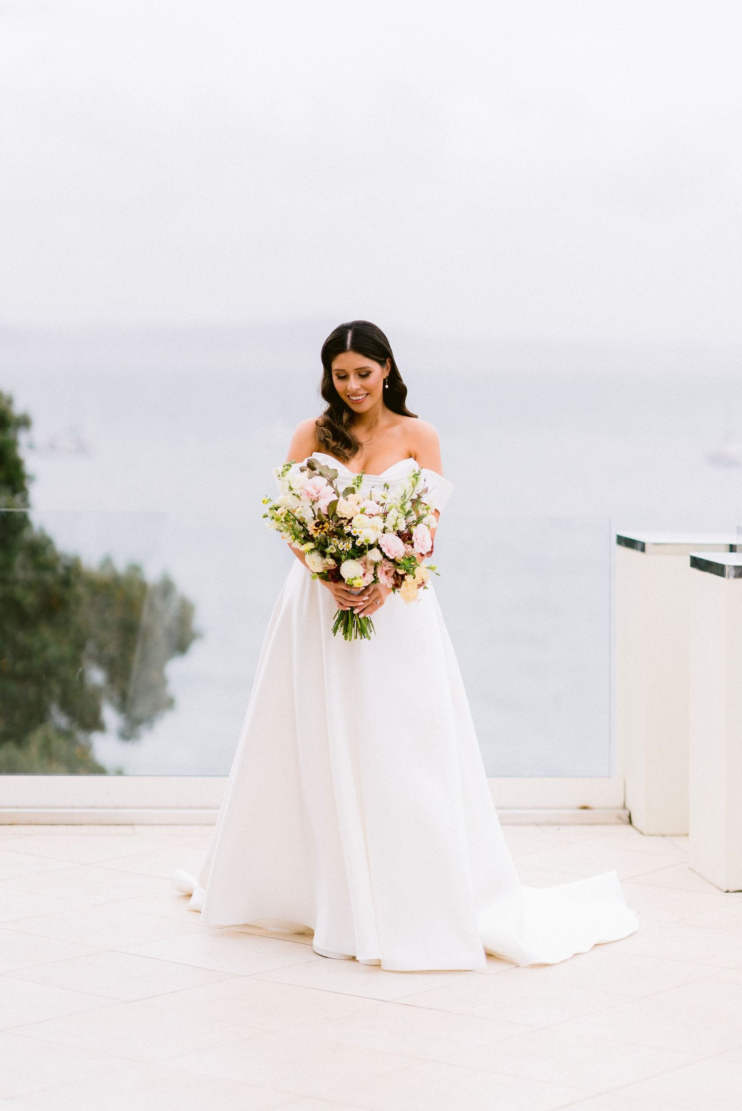 A bride in an elegant off-shoulder white gown holds a romantic blush and white floral bouquet.