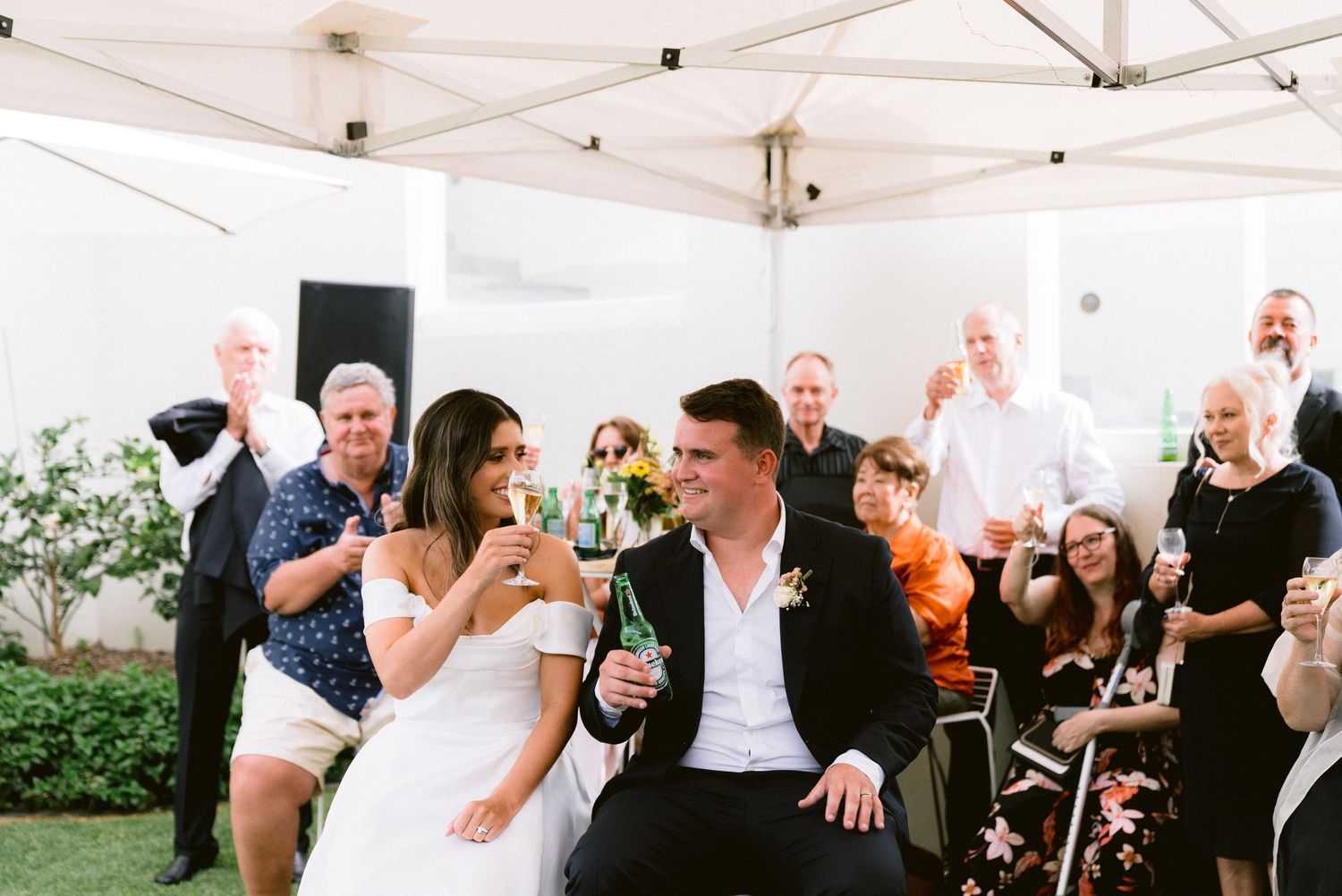 Wedding guests celebrate under a white tent during an outdoor reception.