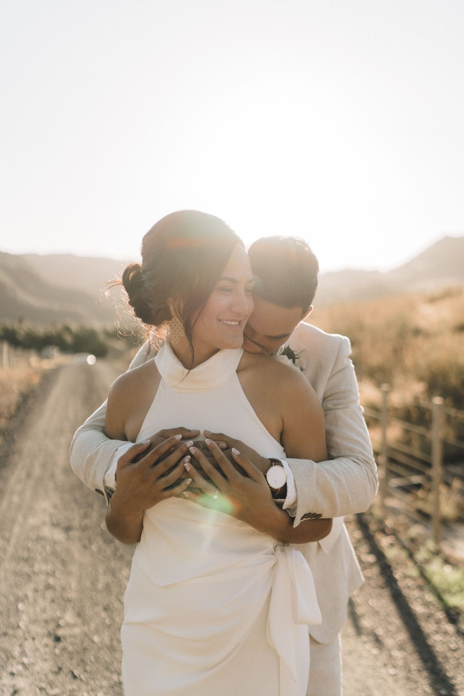 Intimate moment between couple in wedding attire on rural dirt path during sunset.