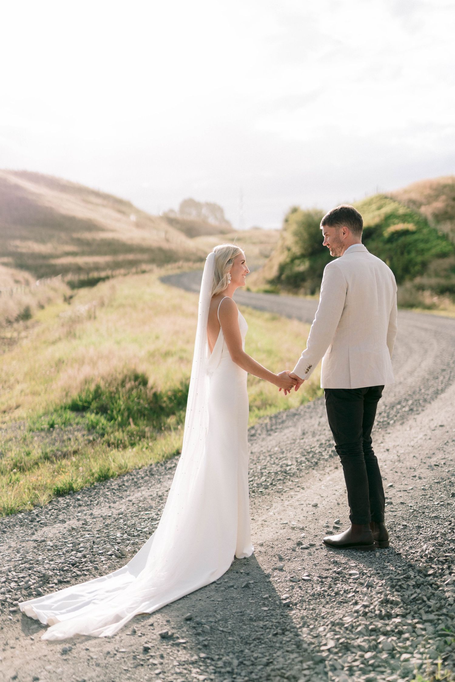 Couple in wedding attire hold hands while walking on scenic mountain path.