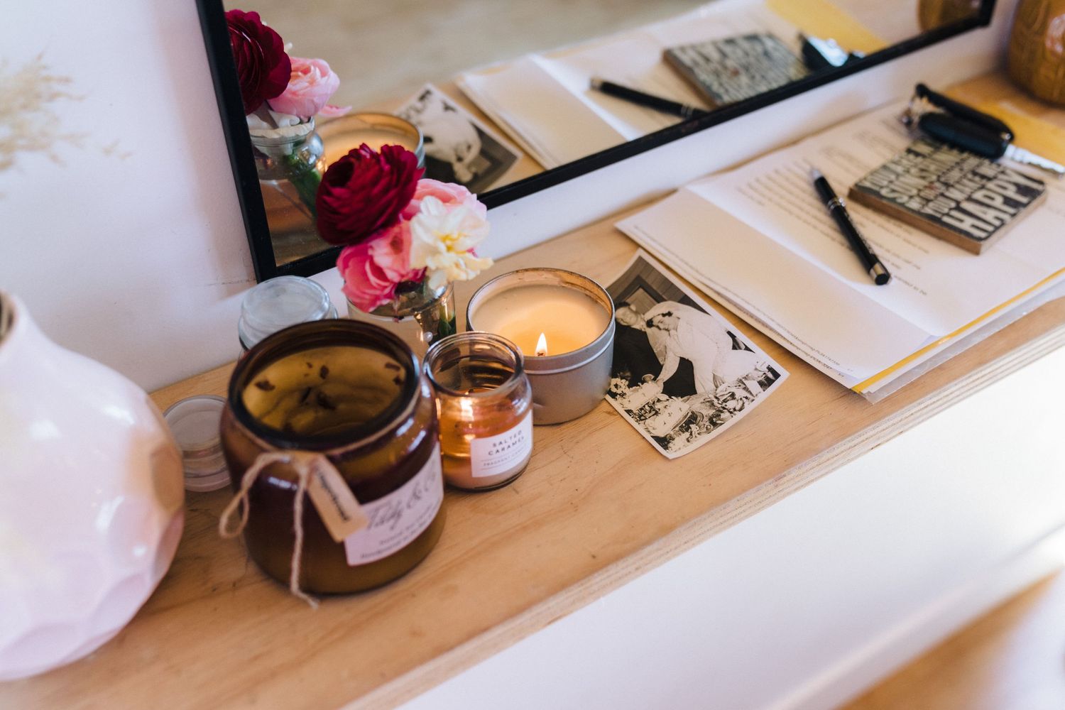 Scented candles and decorative items arranged on a wooden desk with a mirror.