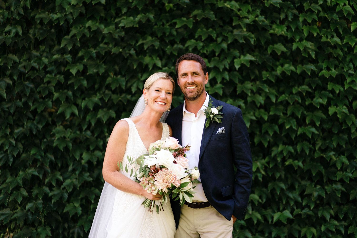 Wedding couple embraces in a romantic outdoor setting with lush green foliage as backdrop.