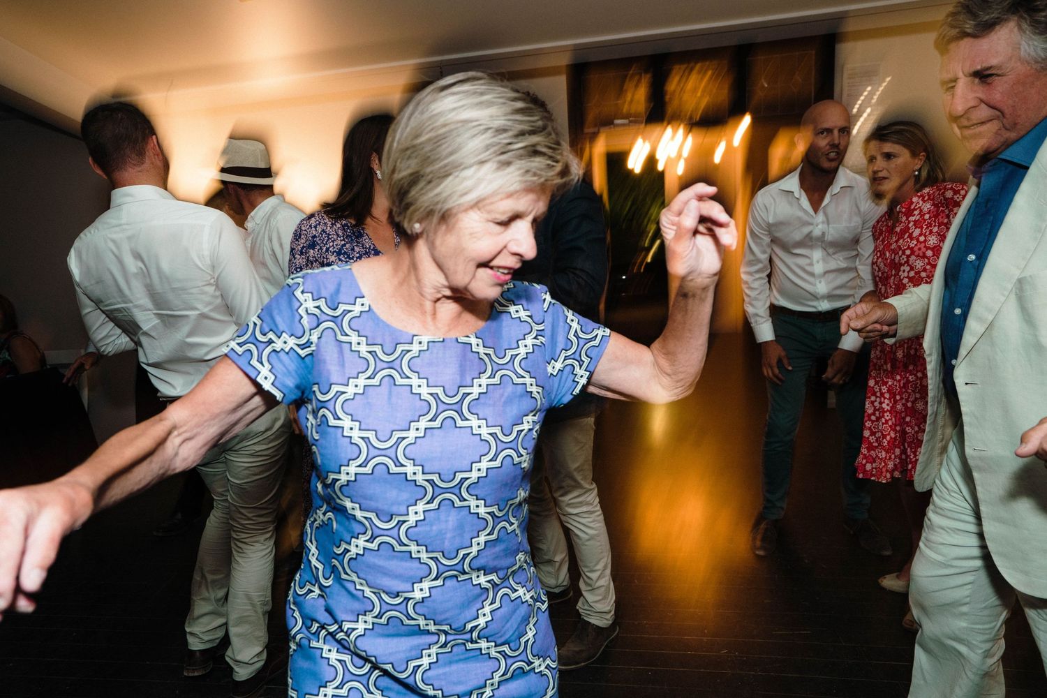 Wedding guests dance and celebrate on a dark dance floor with ambient lighting.