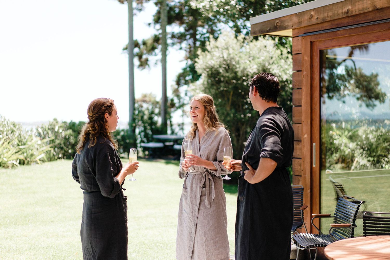 Three people in casual attire having a conversation on an outdoor patio with scenic views and greenery in the background.