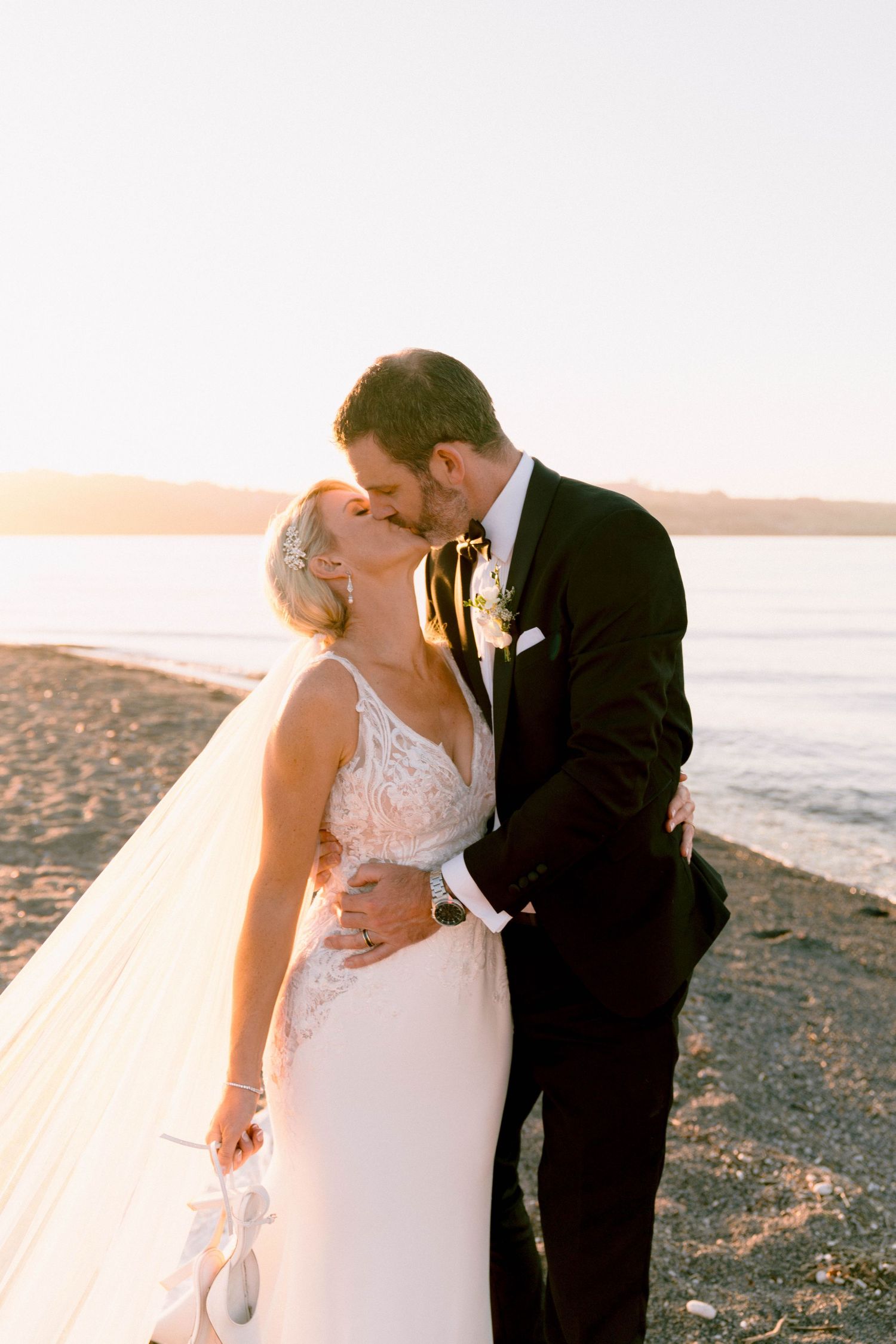 Romantic wedding couple sharing a kiss at sunset on the beach with ocean view and golden light.