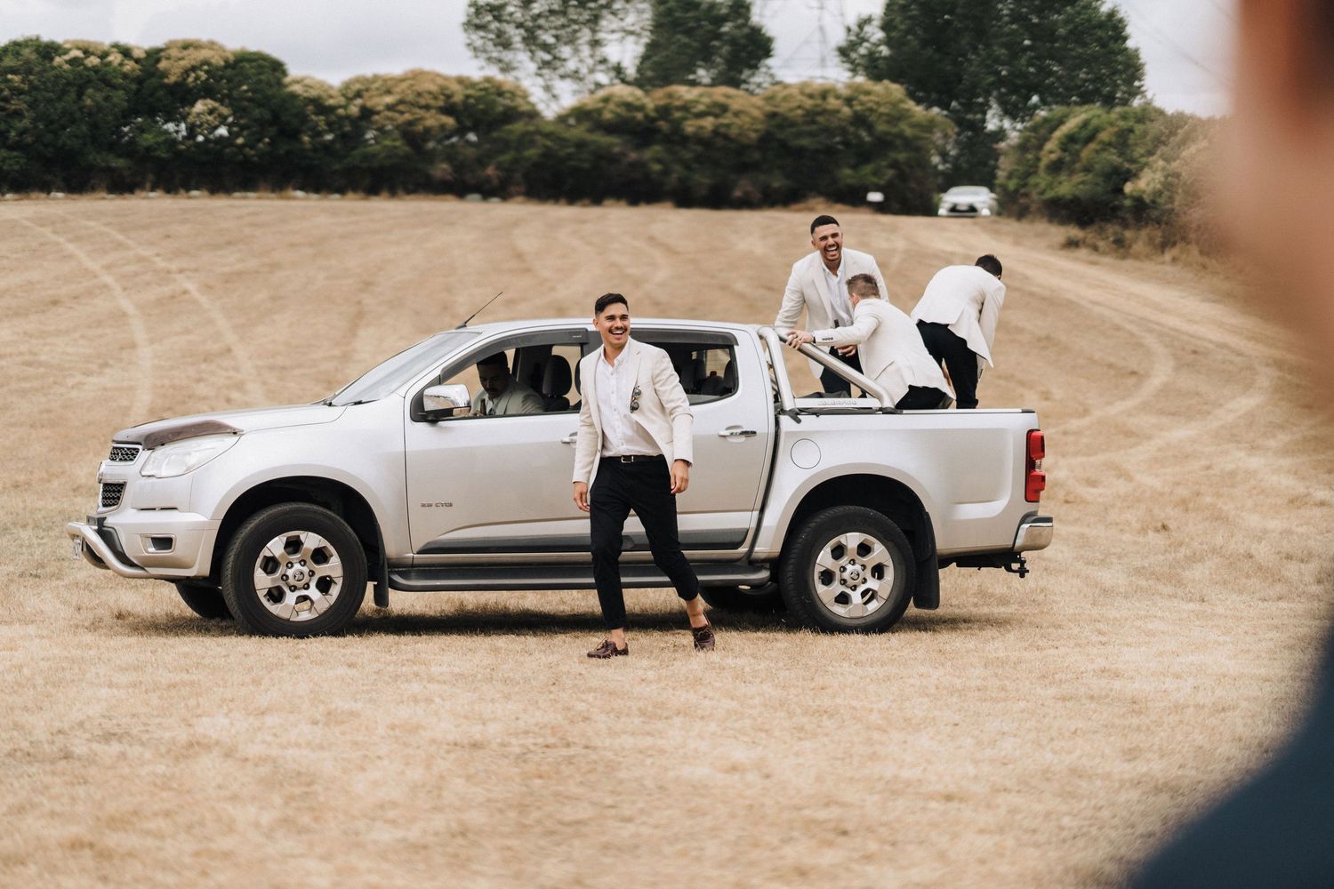 White pickup truck parked in a rural field with people gathered around it.