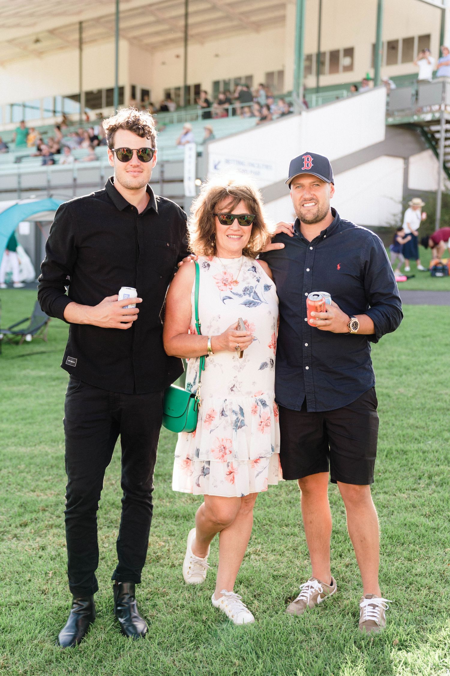 People in casual attire standing together on grass near stadium seating.