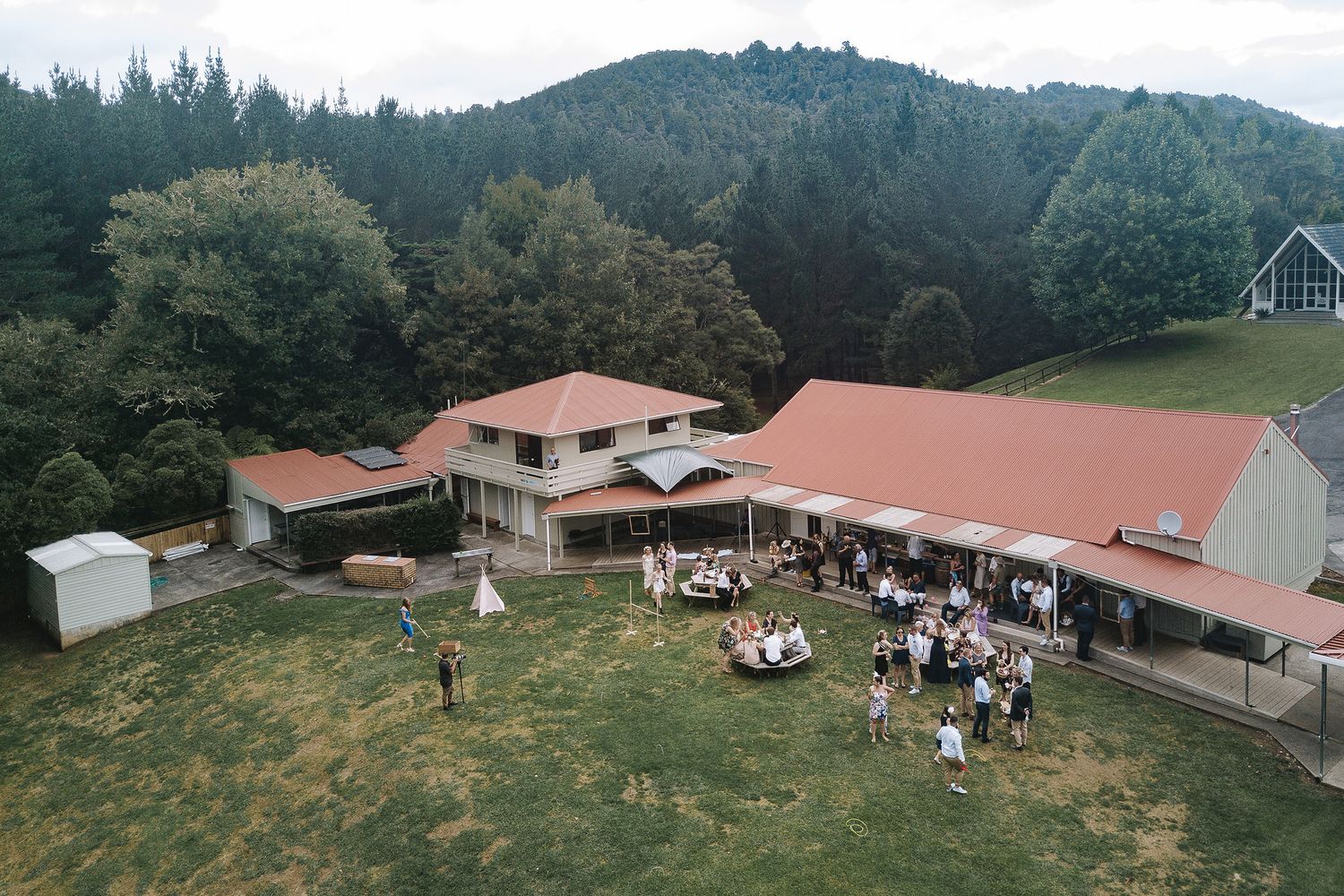Rolling green hillsides dotted with farm buildings and wooden barns surrounded by evergreen forest in a mountainous landscape.