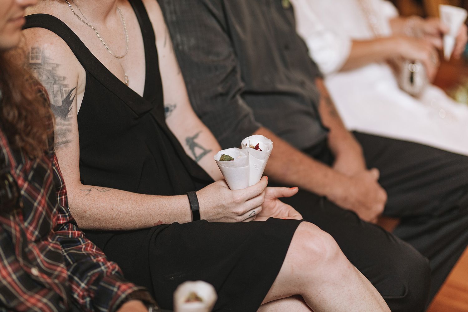 Person in a black dress holds a canned beverage while seated among others at a casual gathering.