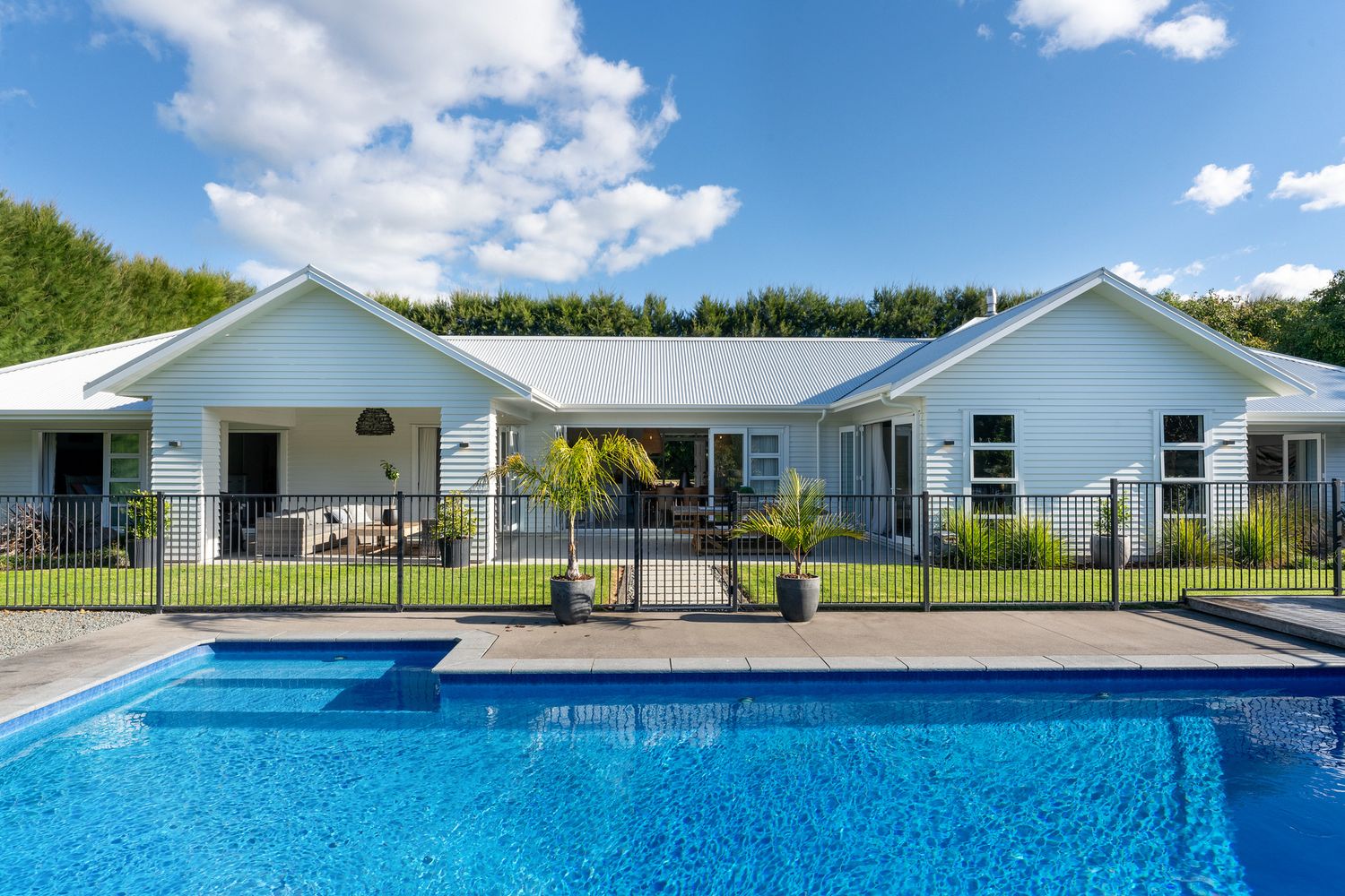 Wide-angle shot of a luxury swimming pool with white fencing and residential buildings in background.