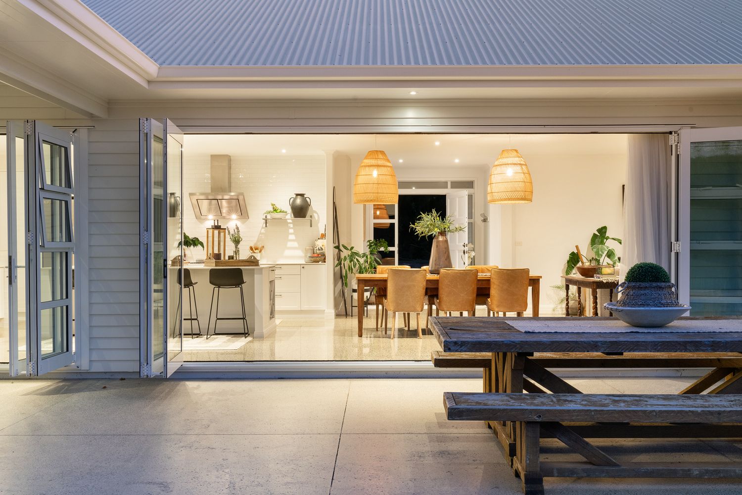 Modern indoor-outdoor living space with bifold doors opening to a picnic bench on the patio at dusk.
