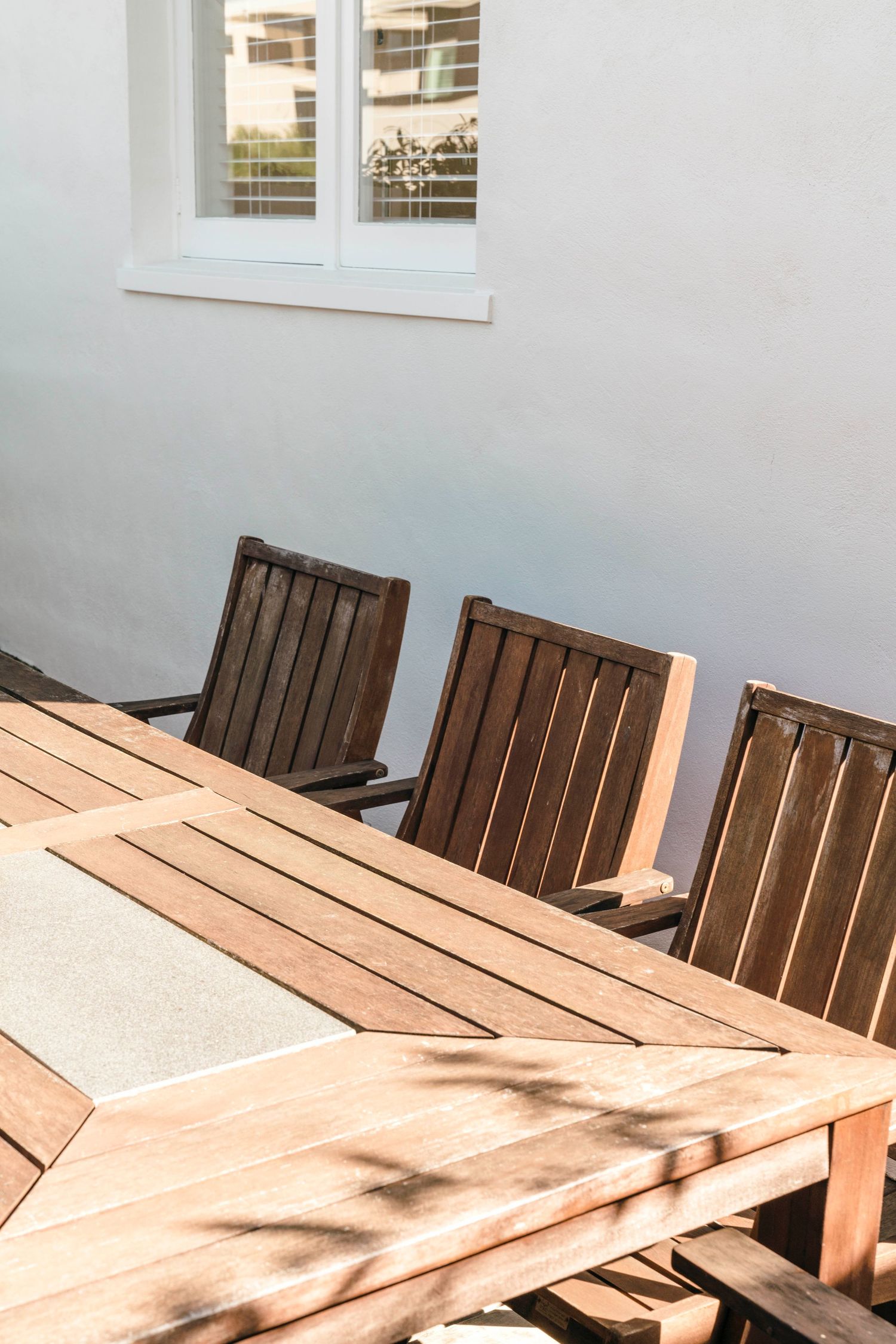Wooden outdoor dining furniture casting shadows on a concrete patio.