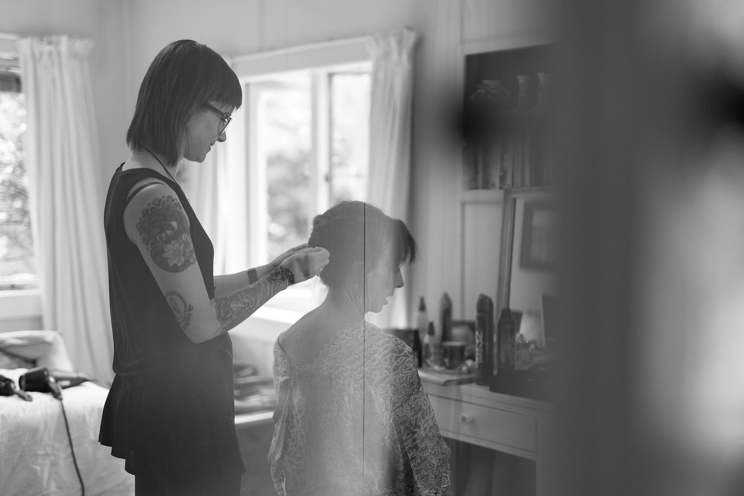 Black and white photo of a hairdresser working in a salon with natural light streaming through windows.