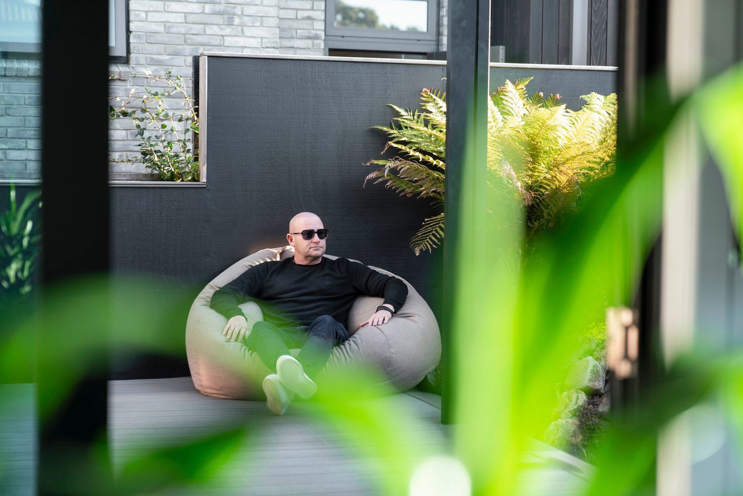 Someone relaxes in a round outdoor chair on a modern patio with plants in the foreground.