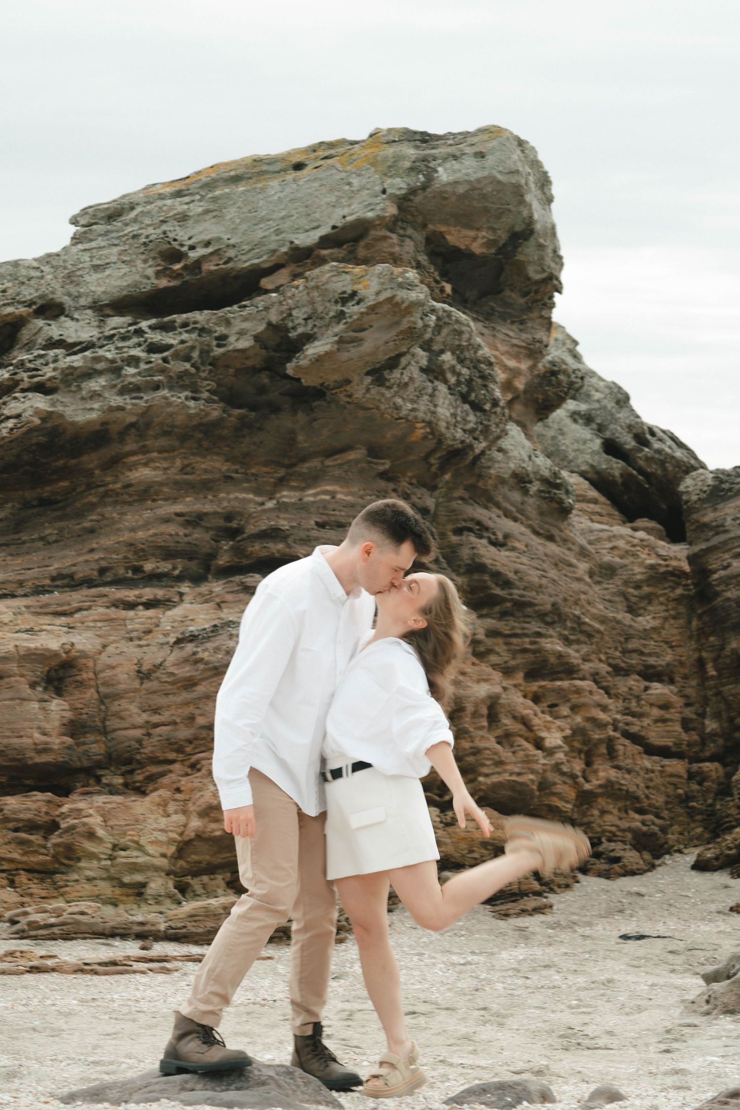 Romantic moment between couple in white on rocky shoreline.