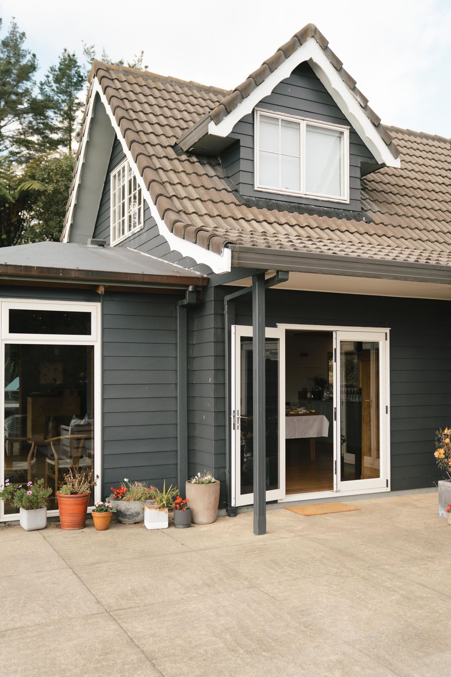 Modern gray house exterior with brown tile roof and sliding glass doors features potted plants along concrete patio.