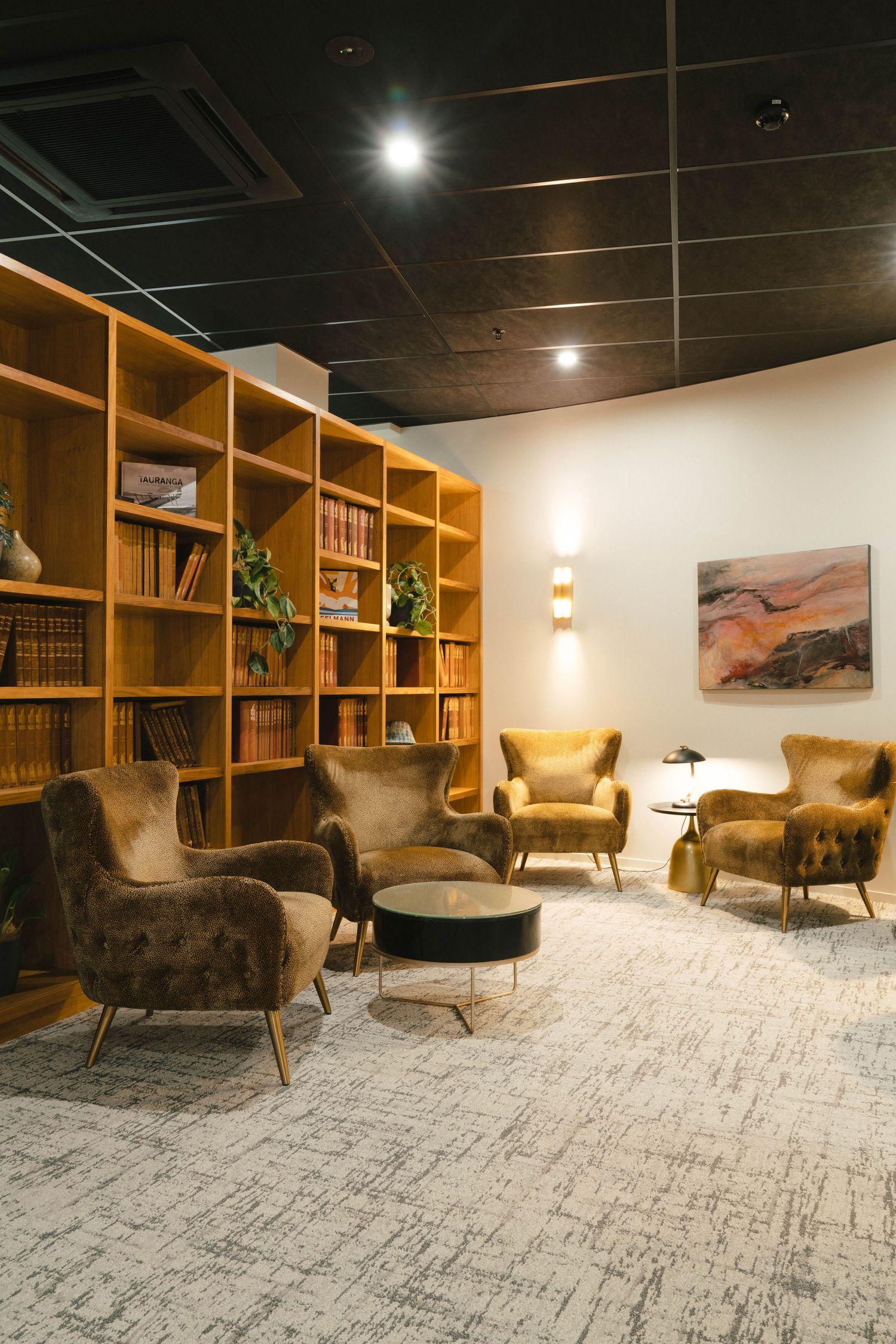 Modern lounge area with wooden bookshelves, comfortable armchairs, and patterned carpet.