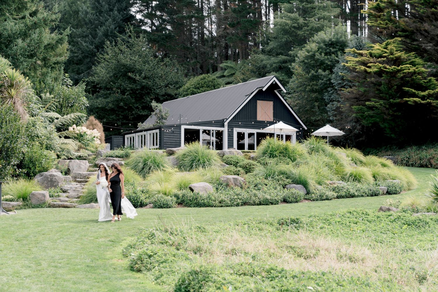 Modern black barn wedding venue surrounded by lush landscaping and evergreen trees.