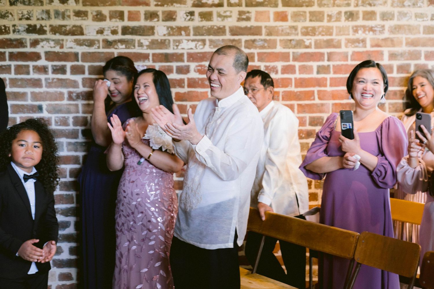 Wedding guests enjoying celebration in brick-walled venue with purple lighting.
