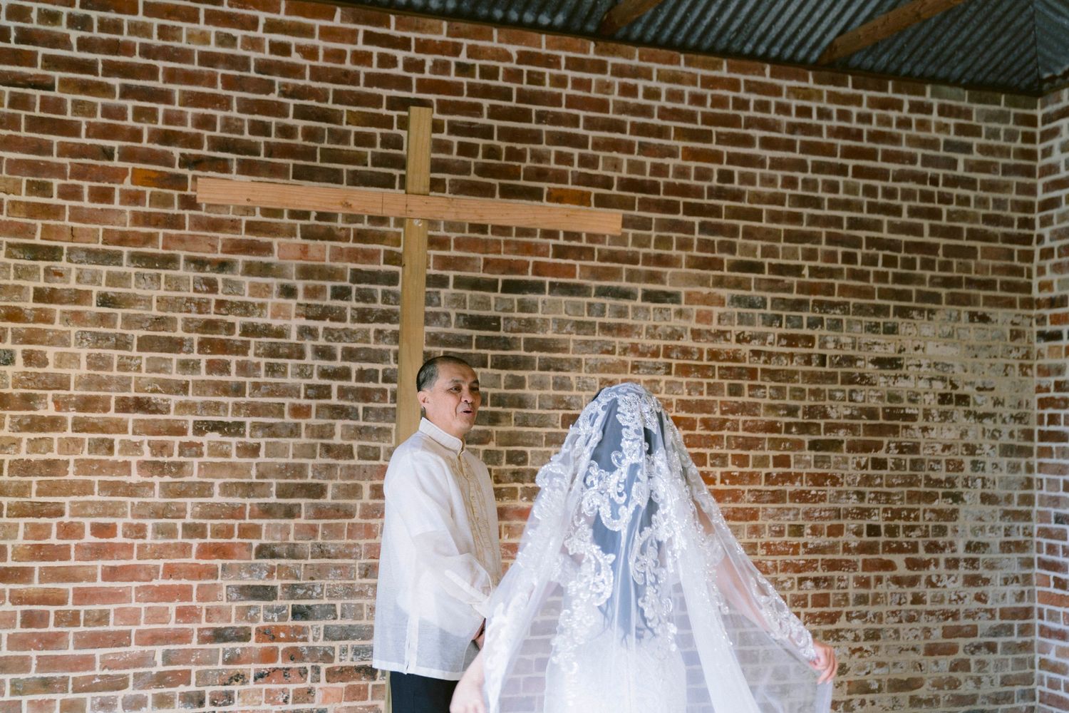 Wedding dress veil detail against exposed brick wall with dramatic lighting and shadows.
