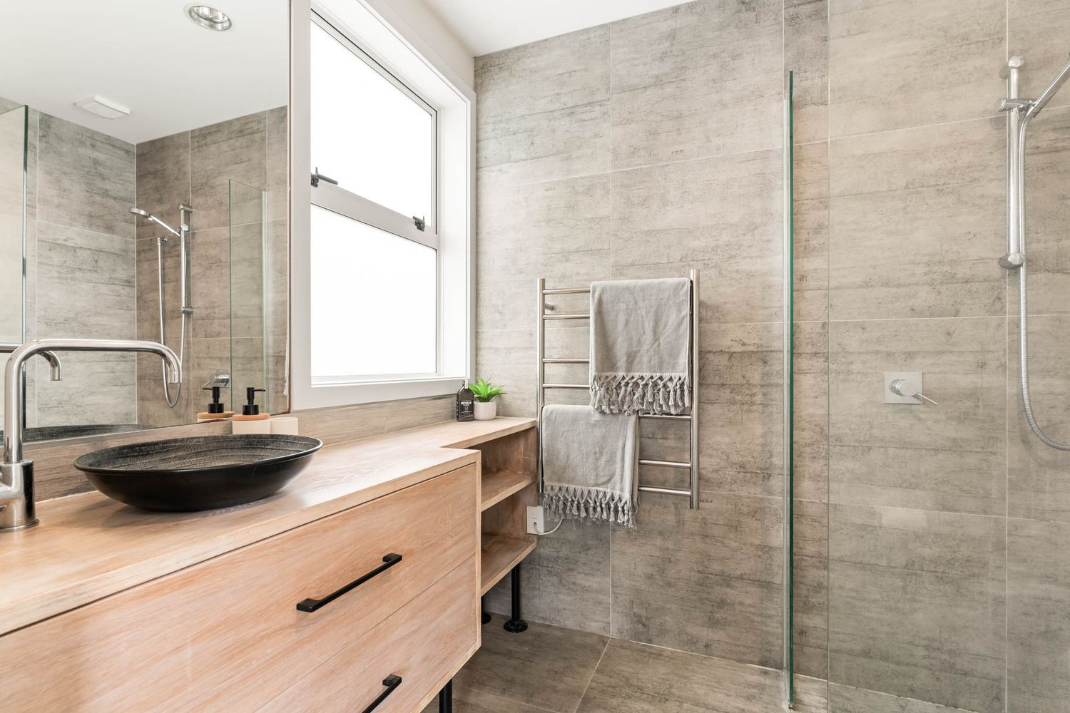 Modern bathroom interior with gray stone tiles and wooden vanity featuring glass shower enclosure.