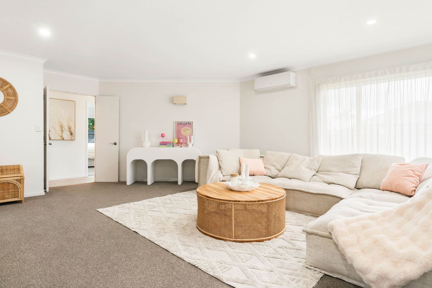 Modern white bedroom interior with natural wood accents, pink throw pillows, and plush carpet flooring.
