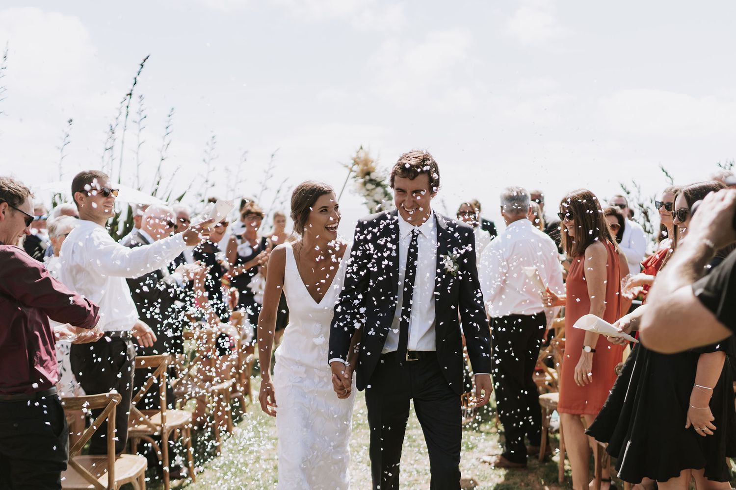 A joyous wedding celebration with confetti being tossed at a newlywed couple during an outdoor ceremony.