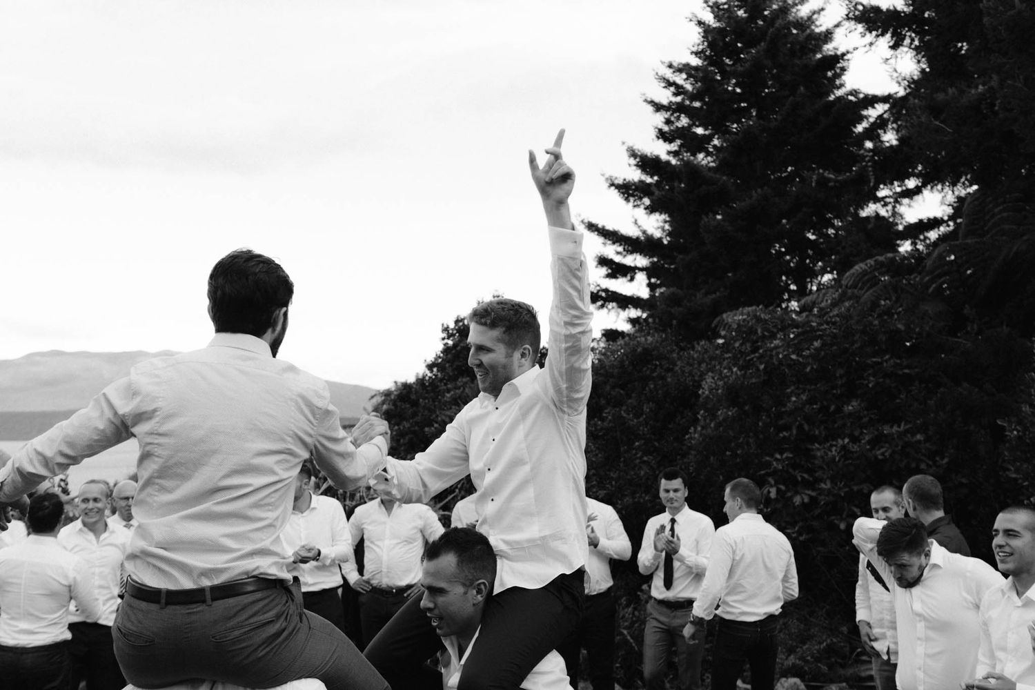 A panoramic series of black and white photos showing people dancing and celebrating outdoors under trees.