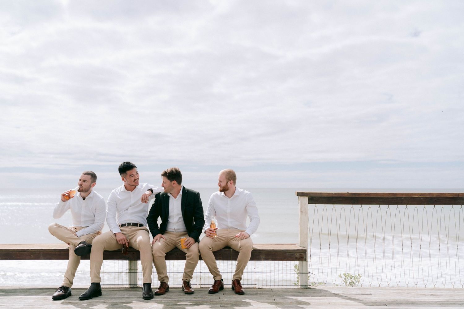 Group of people sit together on a beachside bench enjoying coastal views on a cloudy day.