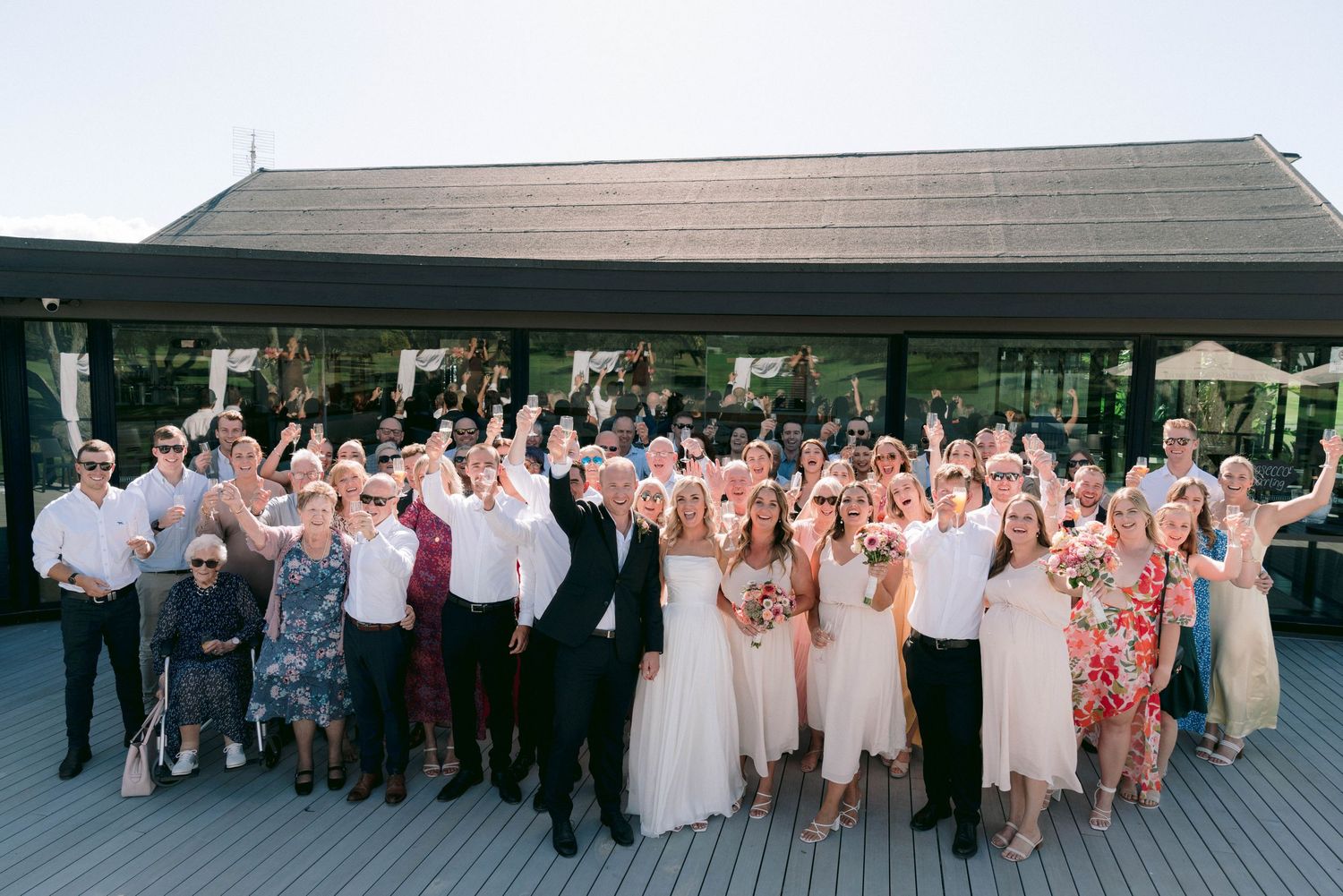 Large group of wedding guests gathered outdoors for a celebratory photo at sunset.