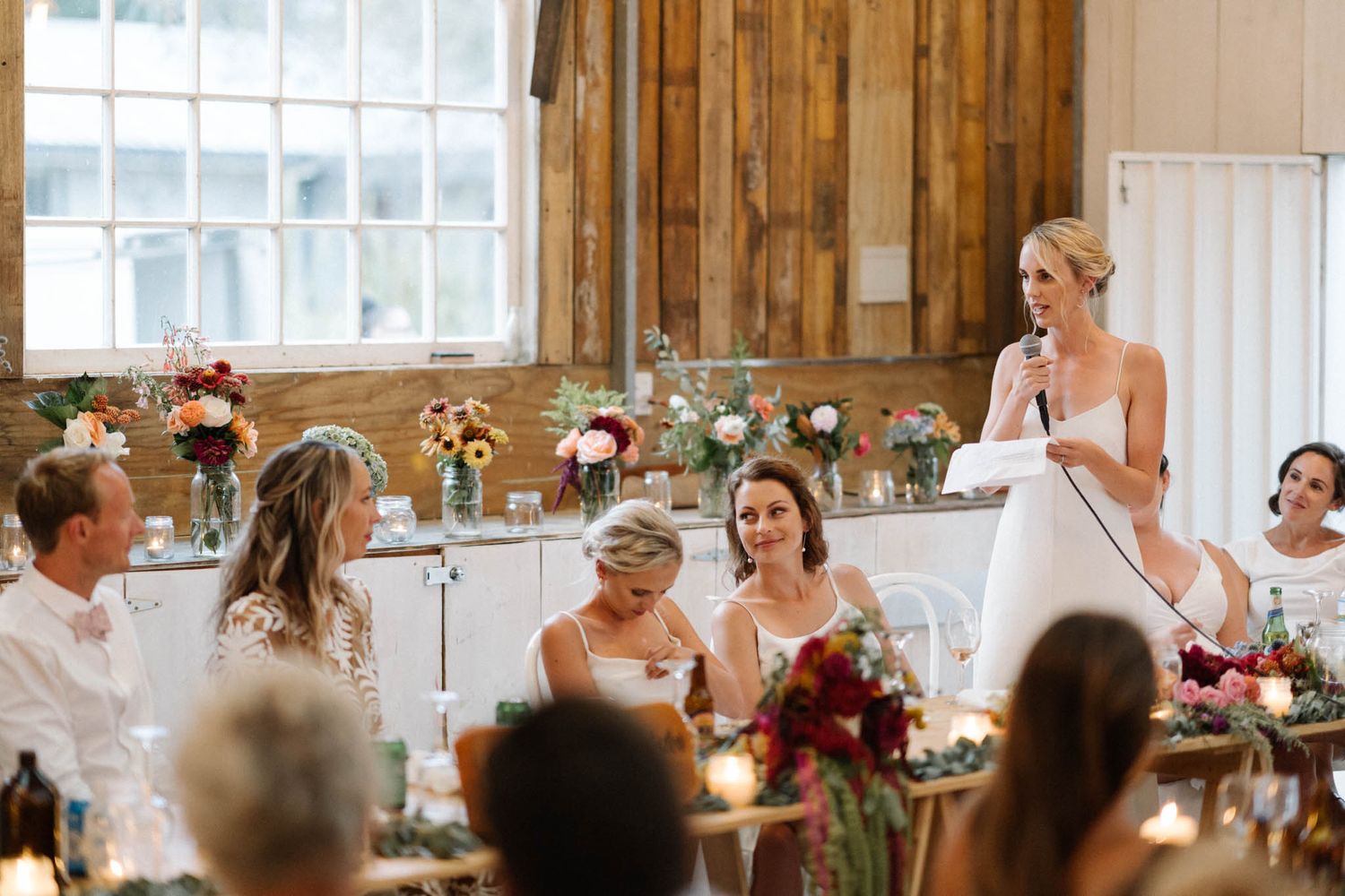 Wedding party celebrates and dances together in a rustic barn venue decorated with romantic floral arrangements.